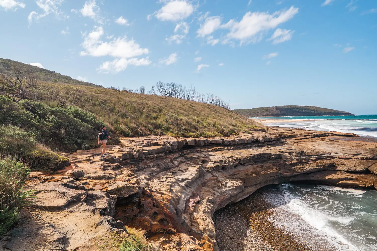 Woman walking along a coastal trail along a high rocky ledge with water below.